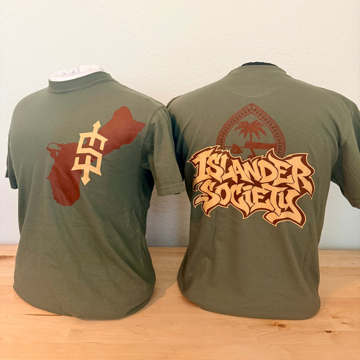 displayed on mannequin torsos showing the front and back designs. The front features an “Islander Society” logo and the back features a large graphic design. 